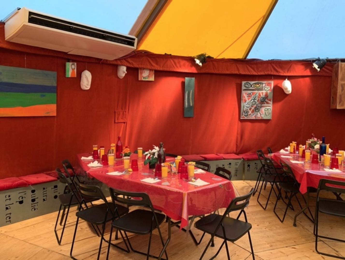 Sous le petit chapiteau, les tables sont mises au cordeau. Les murs sont décorés d’œuvres réalisées dans les ateliers.